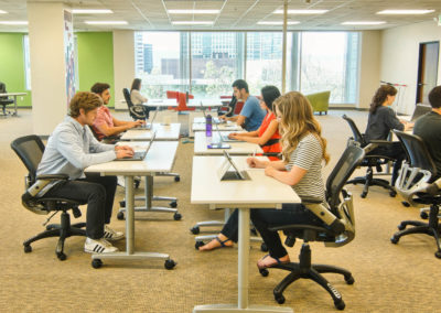 Startup founders sit at desks in the centre of a brightly coloured office space.